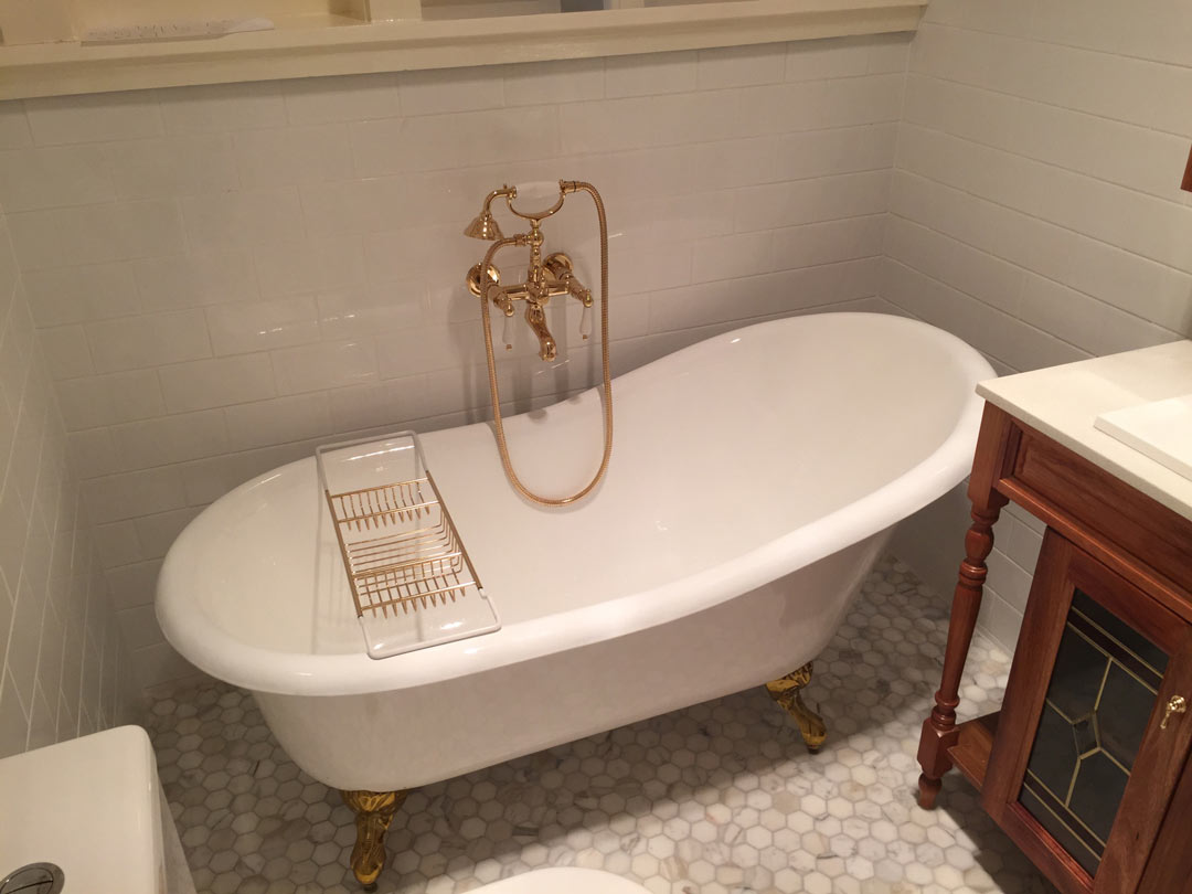 Vintage clawfoot bathtub with golden faucets against a white tiled wall