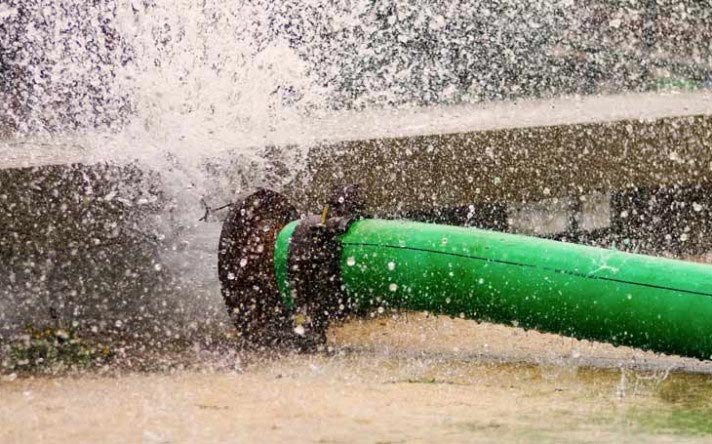 Burst green water pipe with water spraying out.