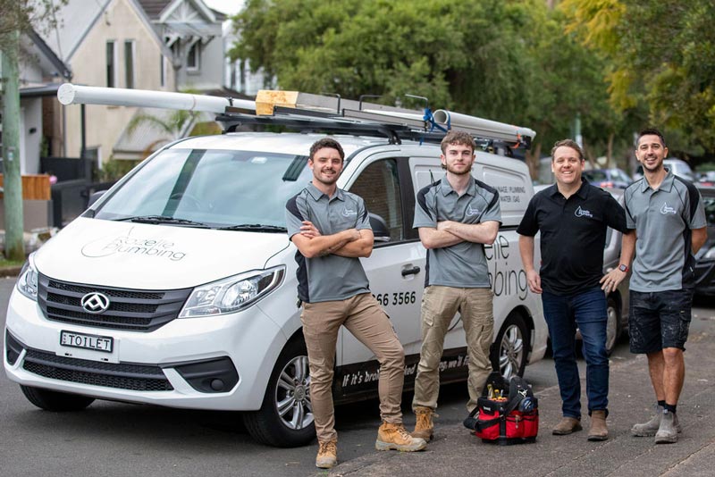 Four workers standing in front of a white van with plumbing equipment.